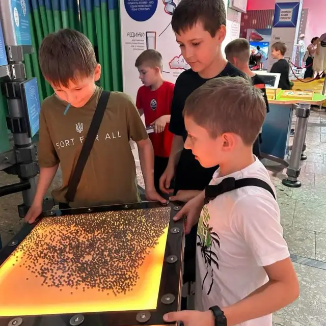 Троє школярів досліджують інтерактивний експонат із рухомими металевими елементами в Музеї науки МАН.