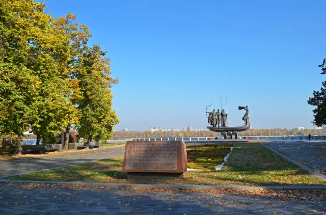 Пам'ятник засновникам Києва — Кий, Щек, Хорив і Либідь на човні — восени, з меморіальним каменем на передньому плані та Дніпром позаду.