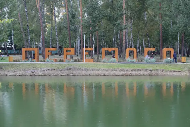 Озеро в парку «Перемога» та великі дерев’яні літери назви парку серед сосен і беріз.