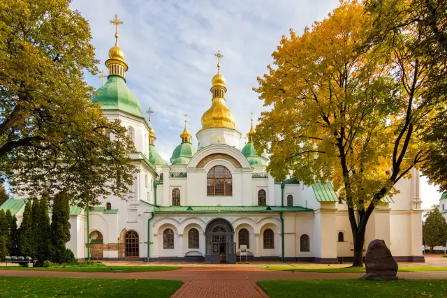 Софійський собор із зеленими дахами й золотими банями серед осінніх дерев.